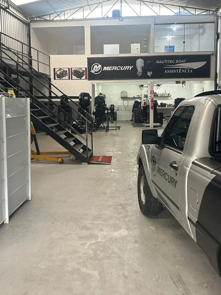 Interior da oficina com o letreiro Nautitec Boat Assistência, motores em cavaletes e a caminhonete de atendimento